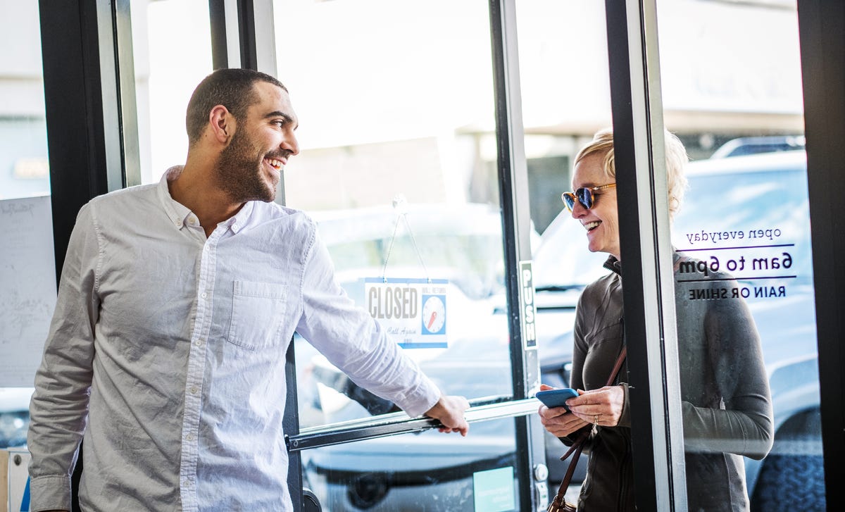 Two people smiling and chatting at the entrance of a store, illustrating a casual conversation that can enhance Spanish vocabulary lessons in real-life situations.