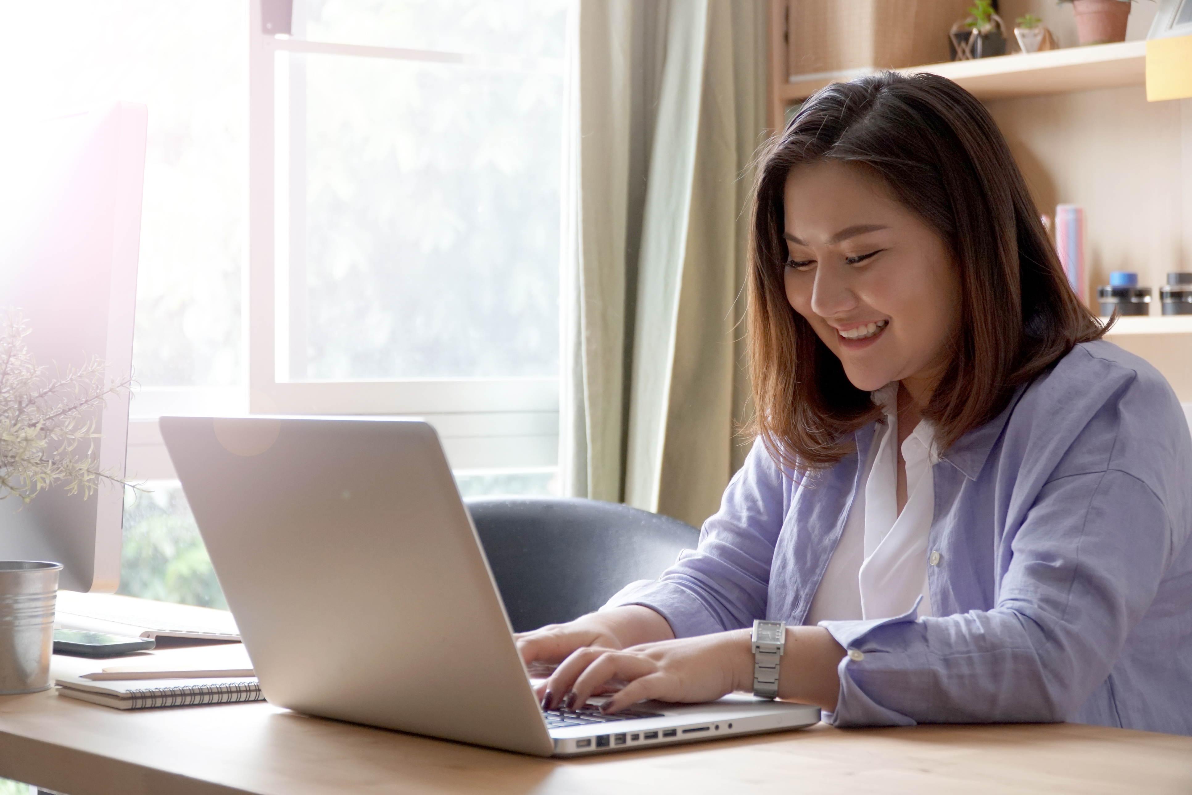 Woman smiling while studying on her laptop, representing flexible online Greek language courses for all proficiency levels.