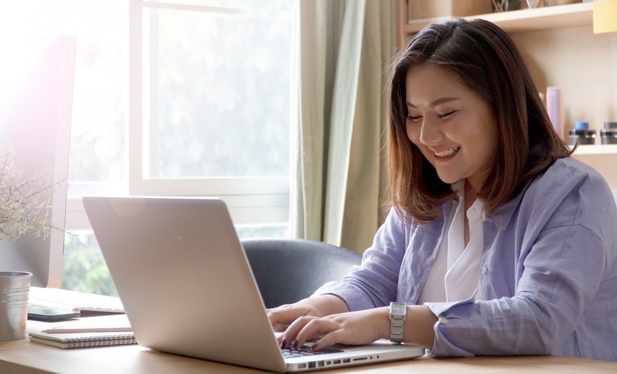 Woman smiling while studying on her laptop, representing flexible online Greek language courses for all proficiency levels.