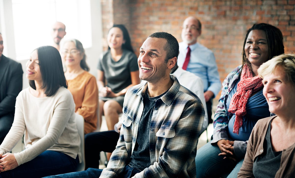 A diverse group of adults smiling and attentively listening during a language class, representing positive Berlitz reviews from satisfied students.