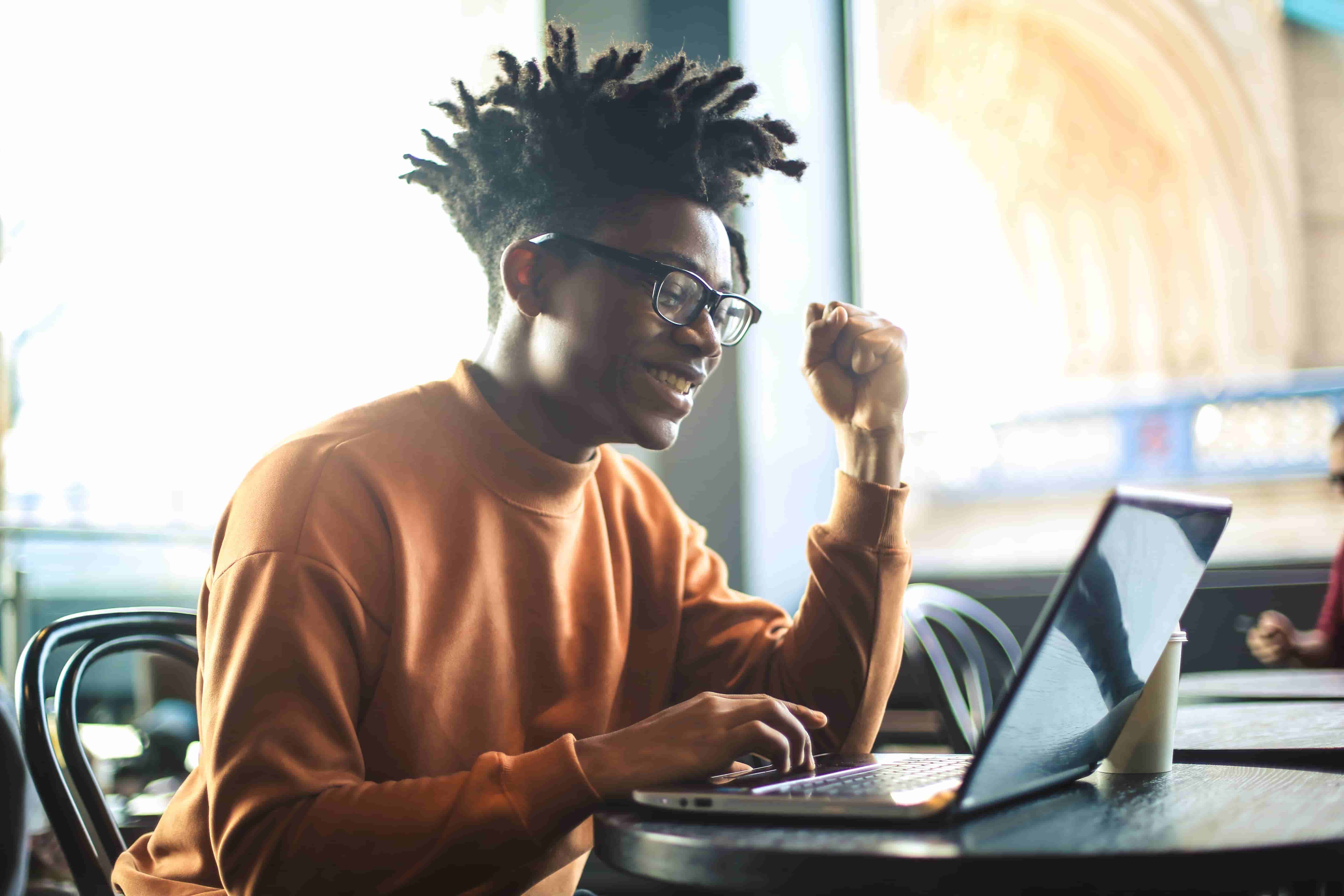 Young man smiling and celebrating while taking an online language speaking test on his laptop, symbolizing success through Berlitz assessment tools.







