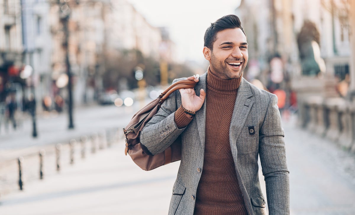 Confident young man smiling while walking in the city, symbolizing success after completing advanced English courses.