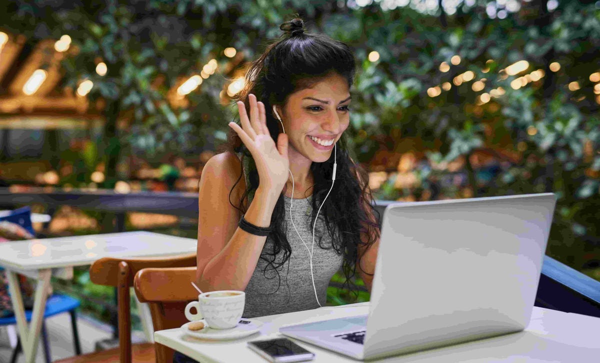 Smiling woman using earphones during a video call on her laptop, representing easy access to virtual classes through the Berlitz login portal.