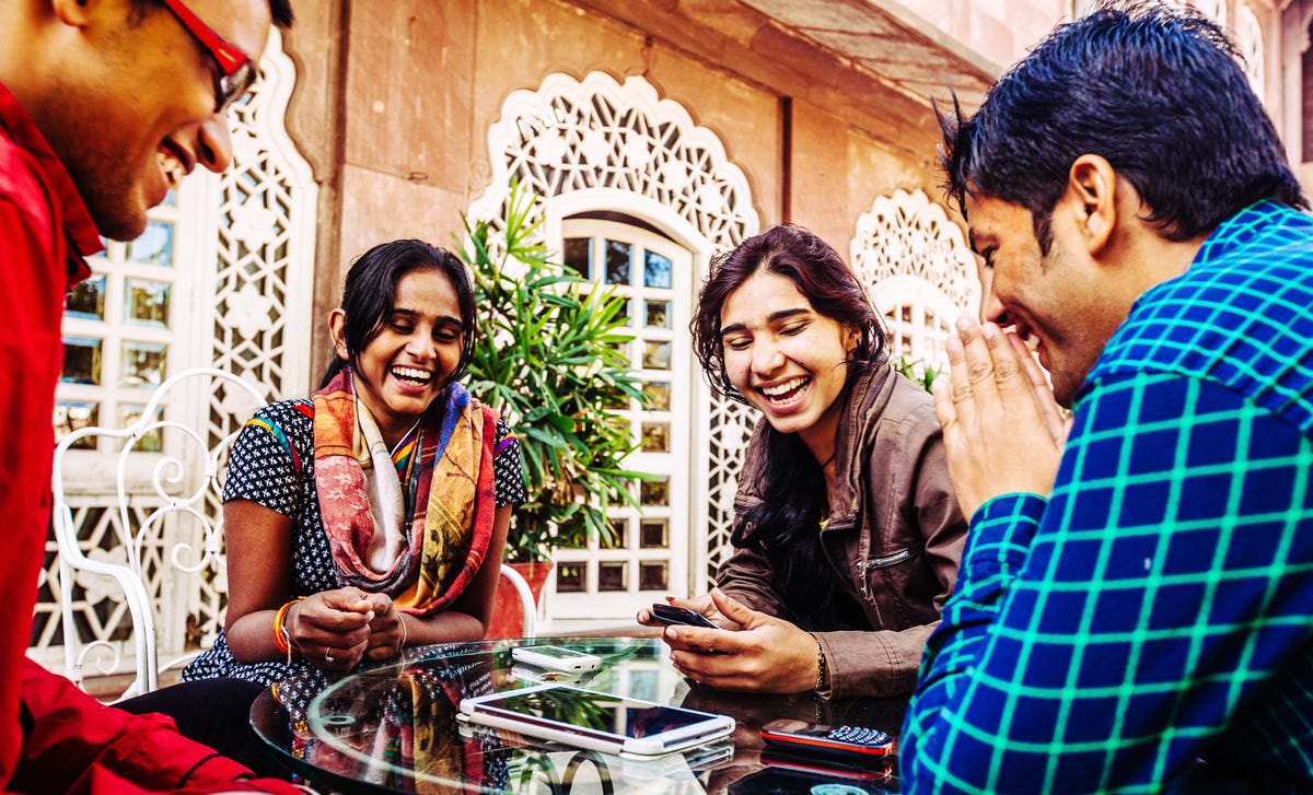 Group of young adults smiling and using mobile devices, possibly attending informal Marathi classes together