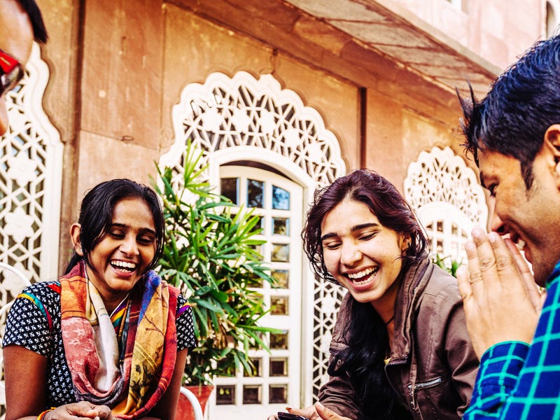 Group of young adults smiling and using mobile devices, possibly attending informal Marathi classes together