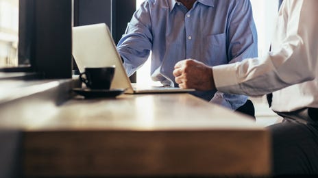 Two senior businessmen discussing work on a laptop, representing the idea of learning Vietnamese online for professionals.