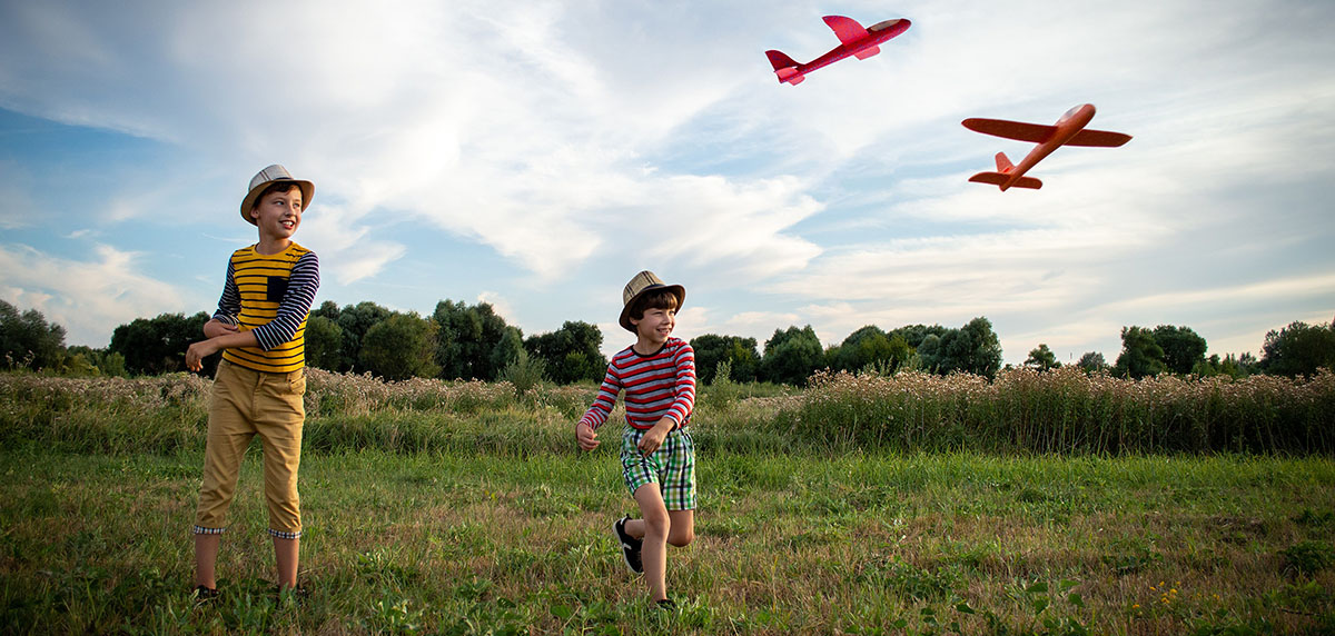 Two young brothers flying paper aeroplanes.