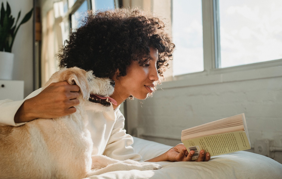 Woman reading Spanish romance novels with her pet dog on her bed.