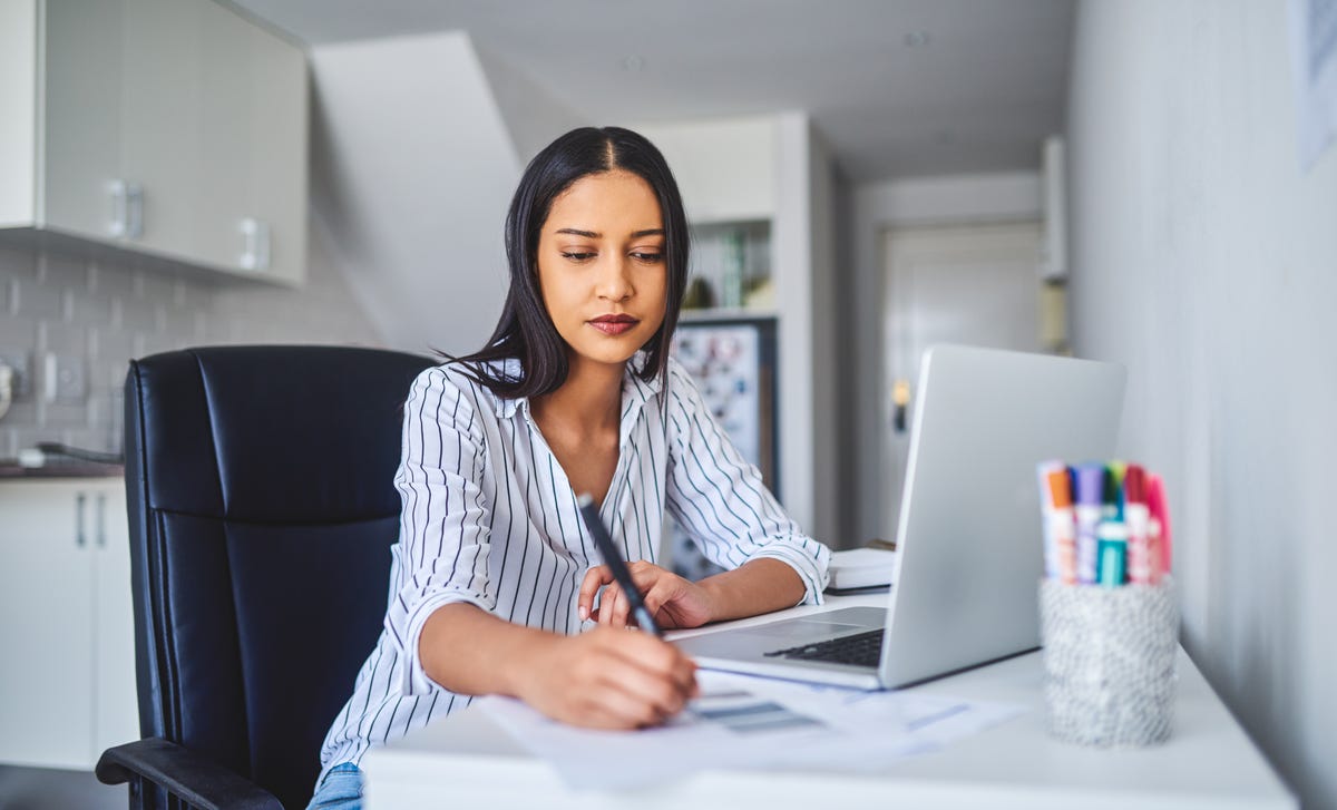 Focused woman studying at home with a laptop and notes to learn Haitian Creole online