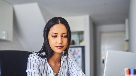 Focused woman studying at home with a laptop and notes to learn Haitian Creole online