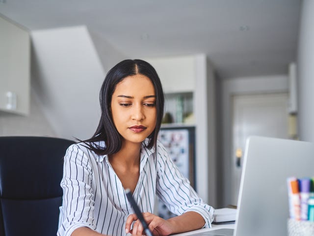 Focused woman studying at home with a laptop and notes to learn Haitian Creole online