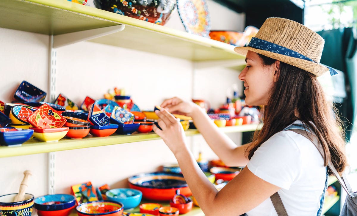 Woman wearing a straw hat browsing vibrant, hand-painted ceramics at a Spanish market stall.