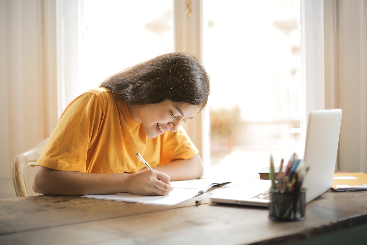 Smiling woman is learning French acronyms with a pen and paper in her office.