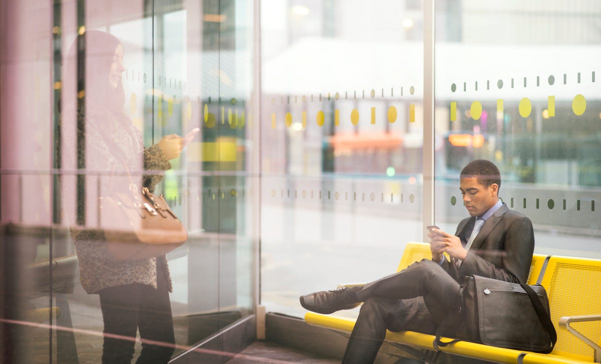 Business professionals using their smartphones at a modern airport lounge, representing the flexibility to learn Latvian online while on the go.