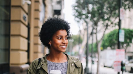 Young woman walking confidently with coffee in hand, smiling after attending an online Korean class.