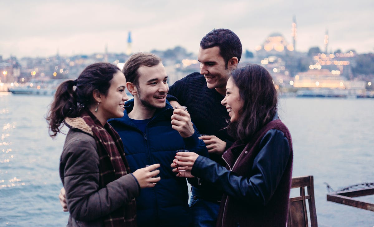 A diverse group of friends enjoying an evening by the water, representing the social and conversational approach to learning Latvian through real-life interactions.