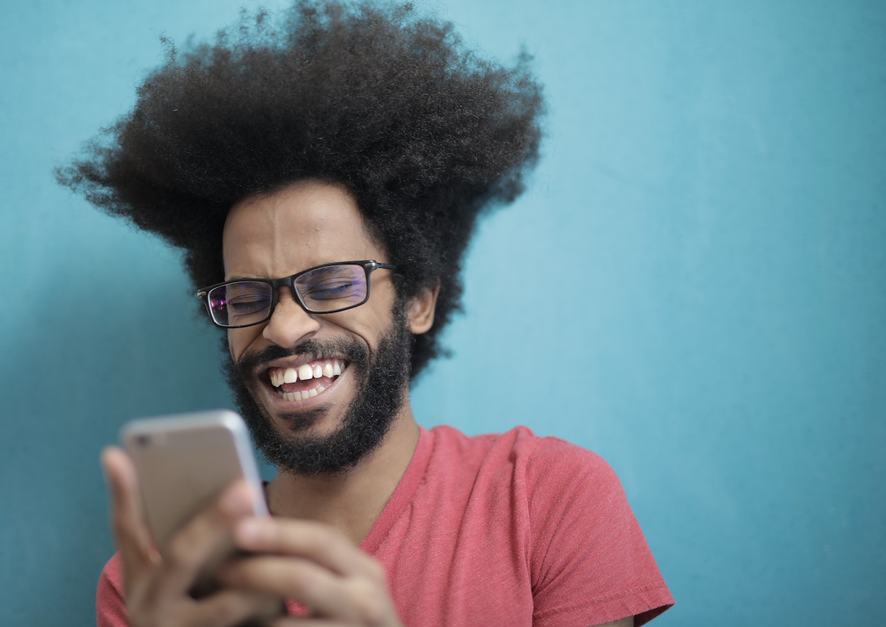 How to say LOL in Spanish with laughing man typing a text with blue wall background.