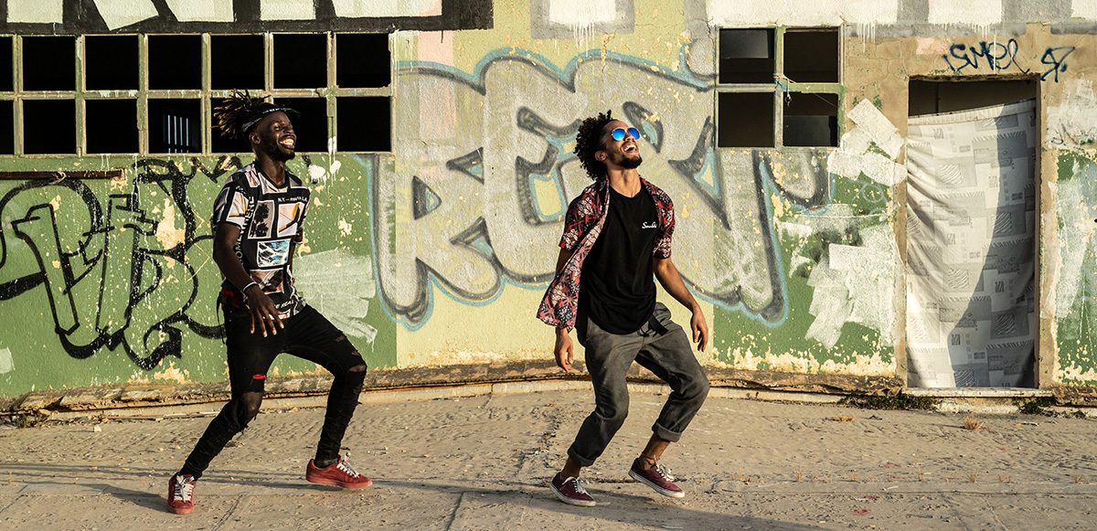 Two men dancing with graffiti in the background.