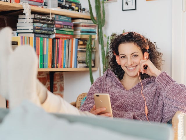 A smiling woman with her feet up is learning a language through music at home with headphones,