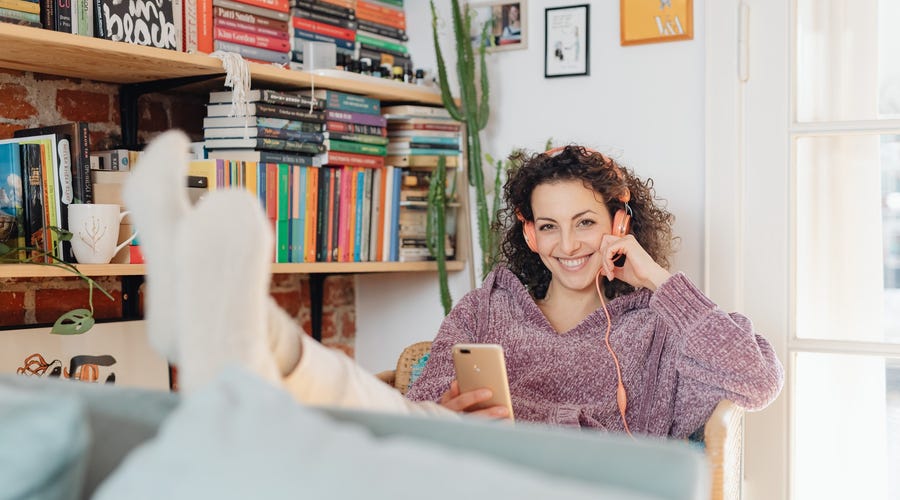 A smiling woman with her feet up is learning a language through music at home with headphones,