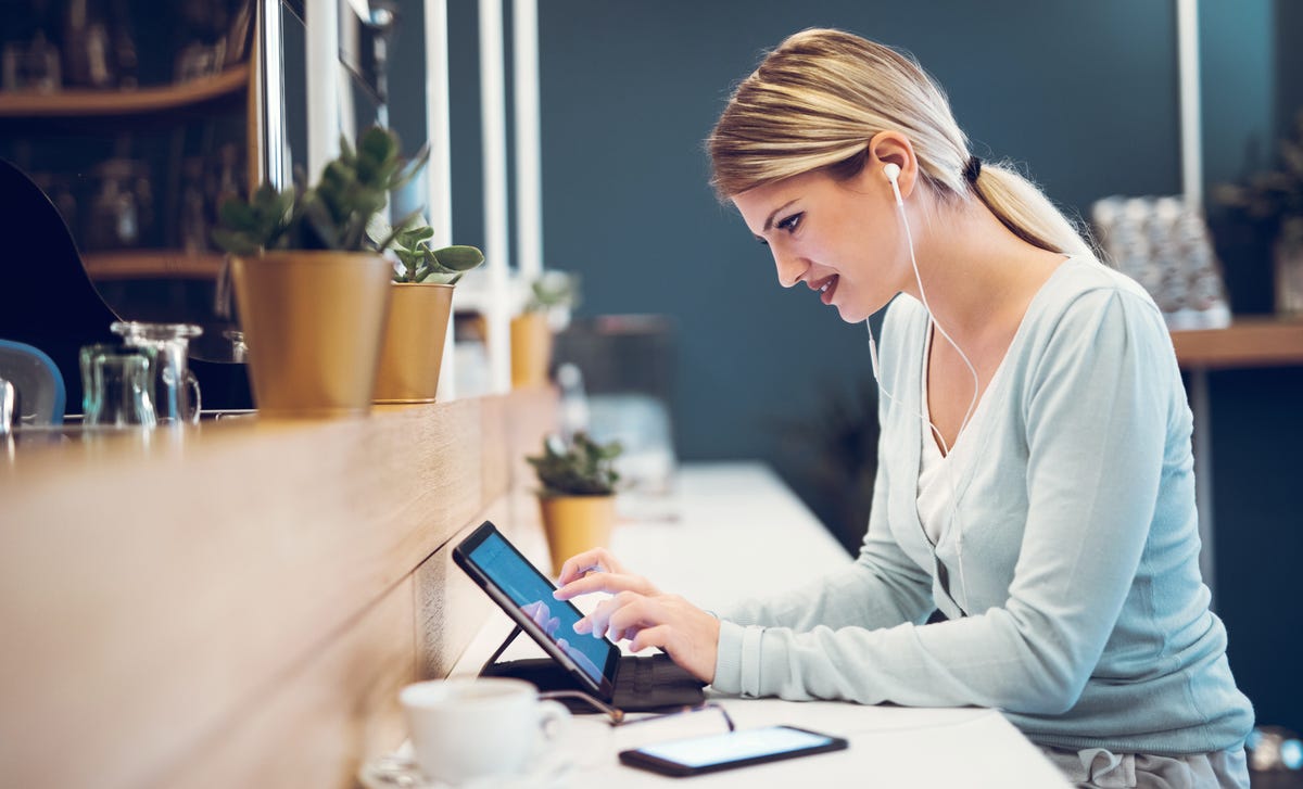 A young woman with earphones engaged in an online Polish lesson at a coffee shop, representing the convenience and flexibility of learning Polish online.
