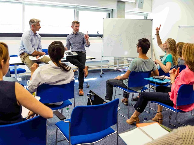 Language training session at Berlitz.com featuring adult students and instructors in an interactive classroom environment with whiteboard instruction.