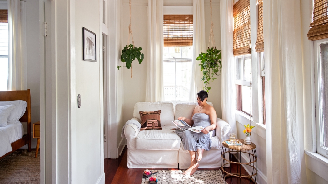 A woman sits on a white couch reading a magazine.