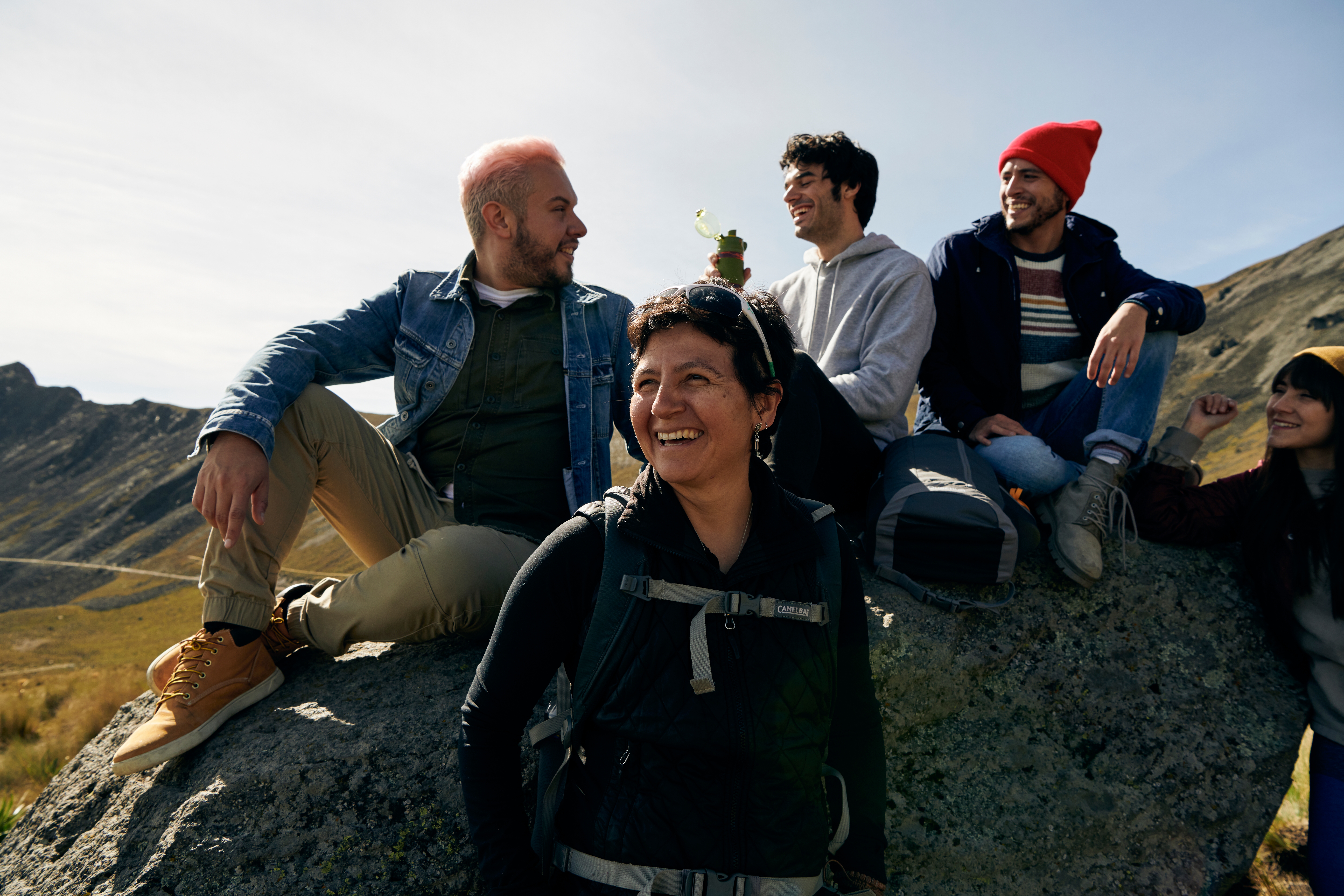 Une hôte d'expérience et ses participants sourient et rient, assis sur un rocher à l'extérieur