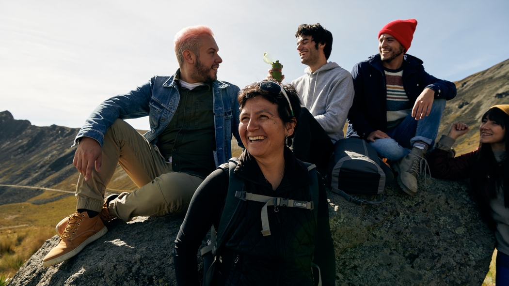 Una organizadora de experiencias y sus participantes están sentados en una roca al aire libre, riendo