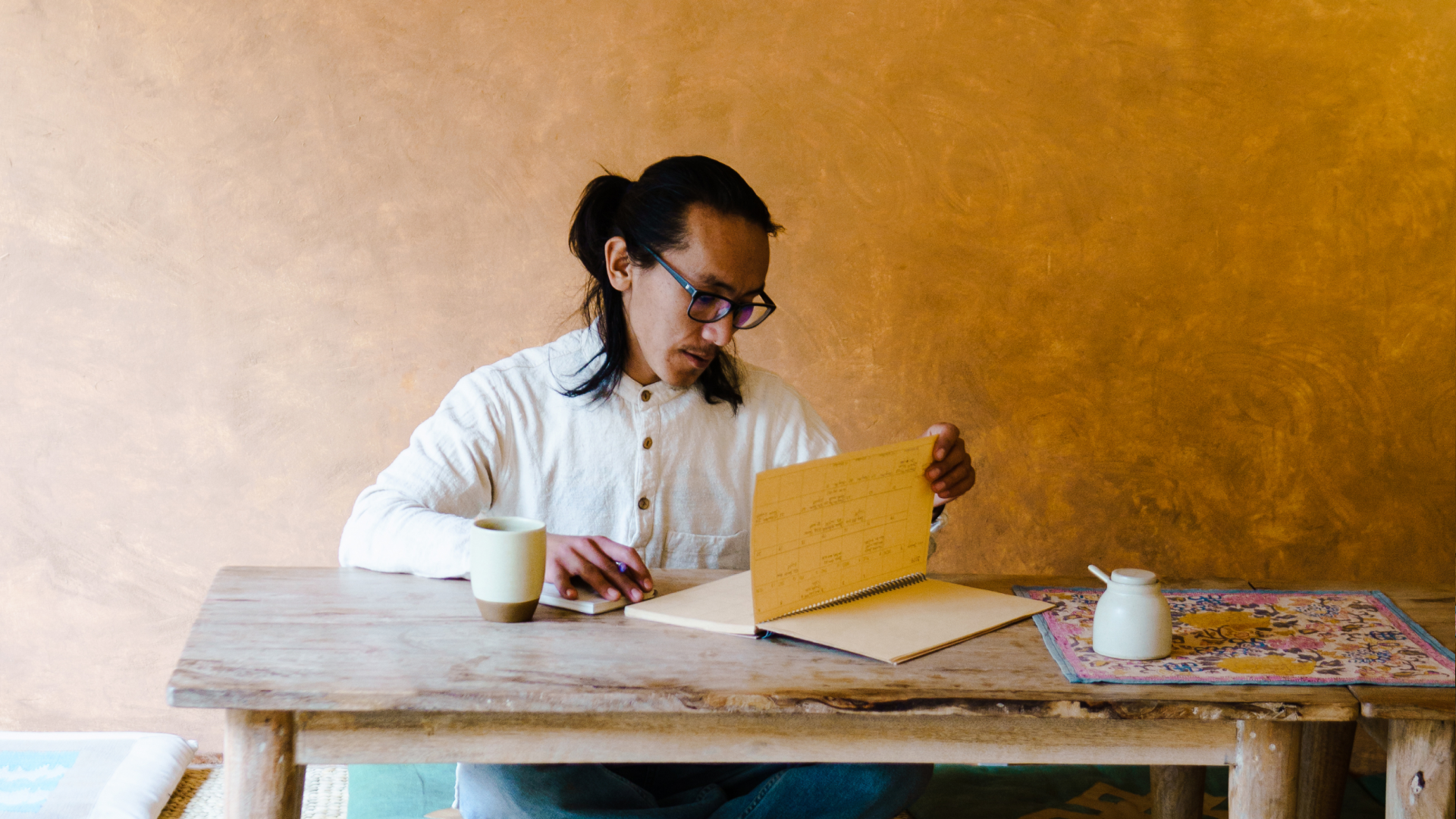 A person sitting cross-legged on the floor reviews a notebook that sits on a low wooden table.