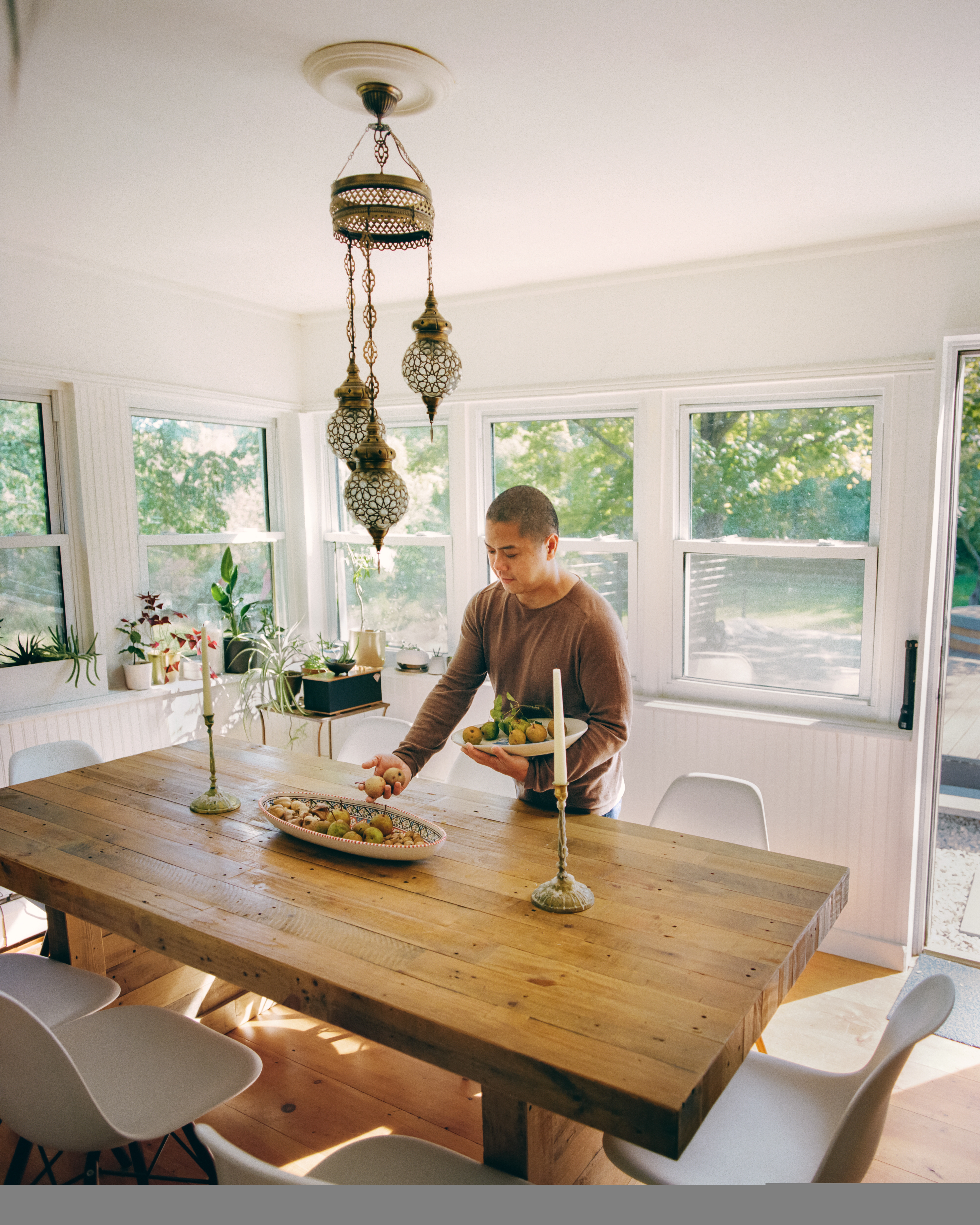 Een persoon staat aan een lange houten tafel en legt fruit in een ovaalvormige schaal in het midden van de tafel.