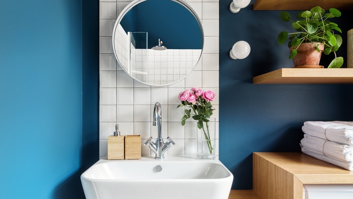 丸い鏡、白いタイルのバックスプラッシュ、オーク材のアクセントを備えた、清潔でモダンなバスルームの洗面台。