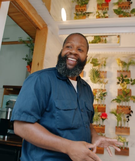Superhost Ansel stands in front of a wall of plants with his reflection in a mirror behind him.