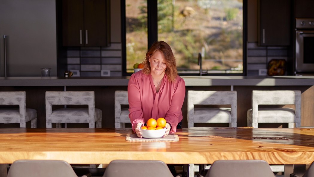 Une femme dispose une corbeille de fruits sur une table ensoleillée.
