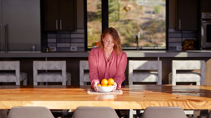 A woman sits at a table in the sunshine with a bowl of fruit.