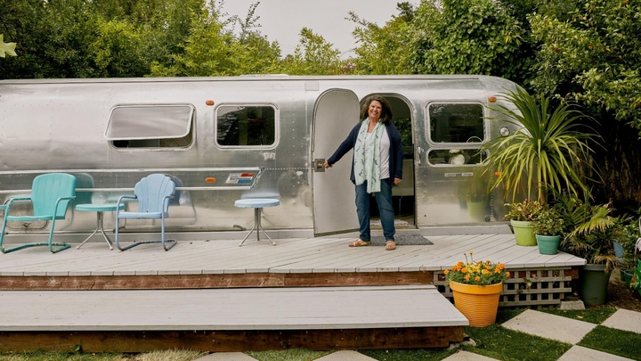 يقف المضيف على سطح خشبي تاركًا باب مقطورة Airstream مفتوحًا، وهو مثال على نوع العقار الفريد من نوعه.
