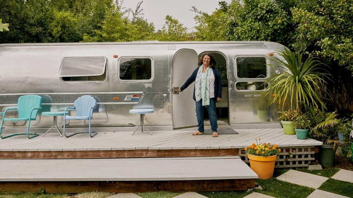 A Host stands on a wooden deck and holds open the door of an Airstream trailer, an example of a unique space property type.