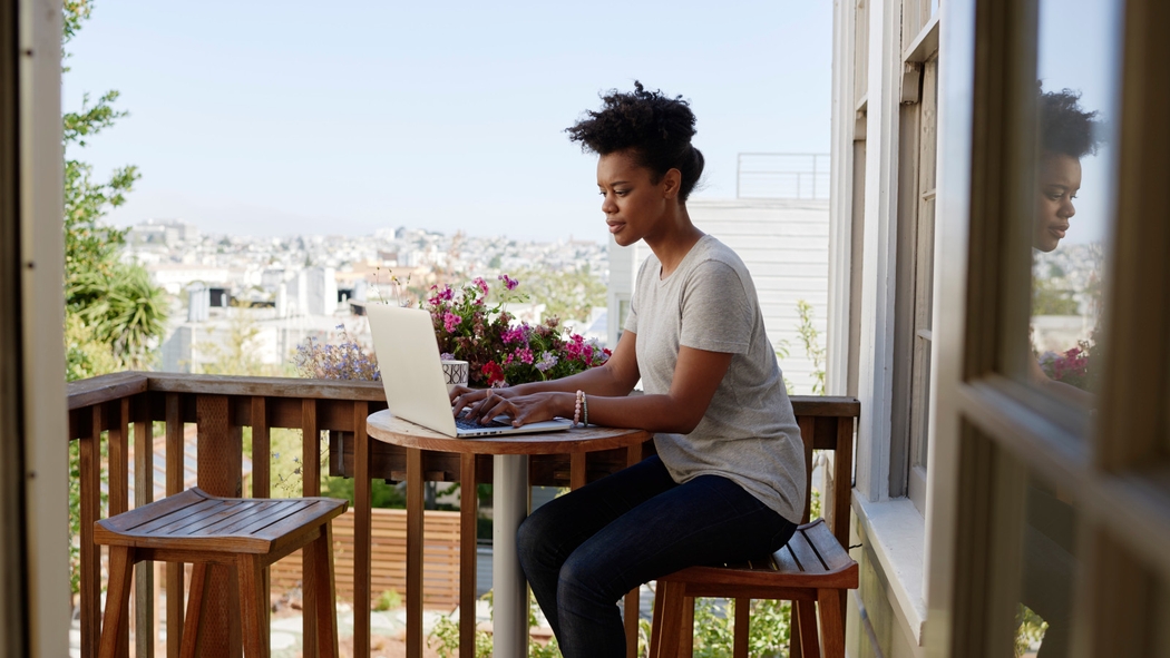 背景是城市街景，一位女性在阳台上工作，她正在用电脑打字