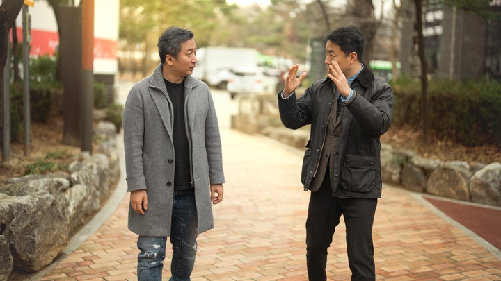 Una persona con un abrigo gris conversa con otra persona con una chaqueta negra en una pasarela.