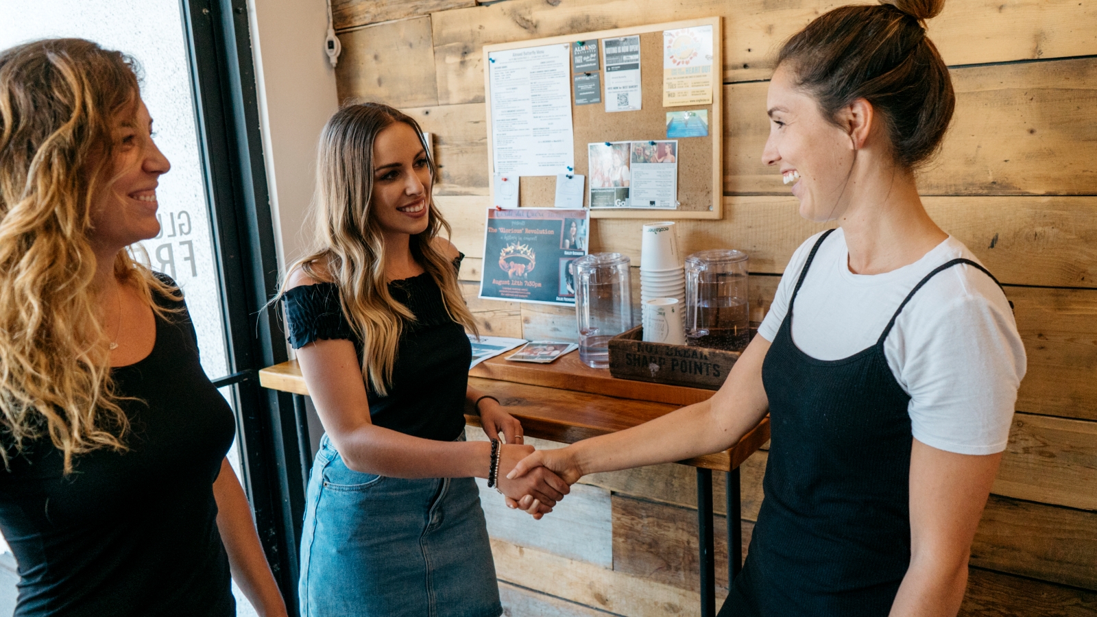 Host in a coffee shop greeting two guests and shaking hands with one of them