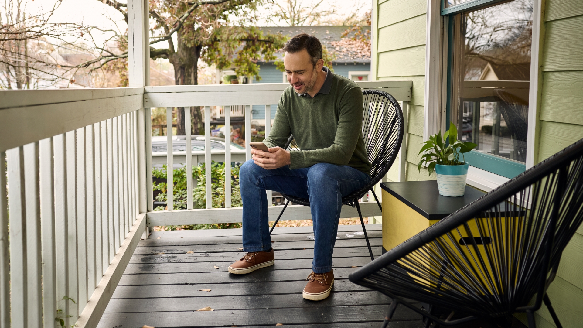 A person wearing glasses looks at a smartphone while seated at a burled wood table. Sun shines through an open window.