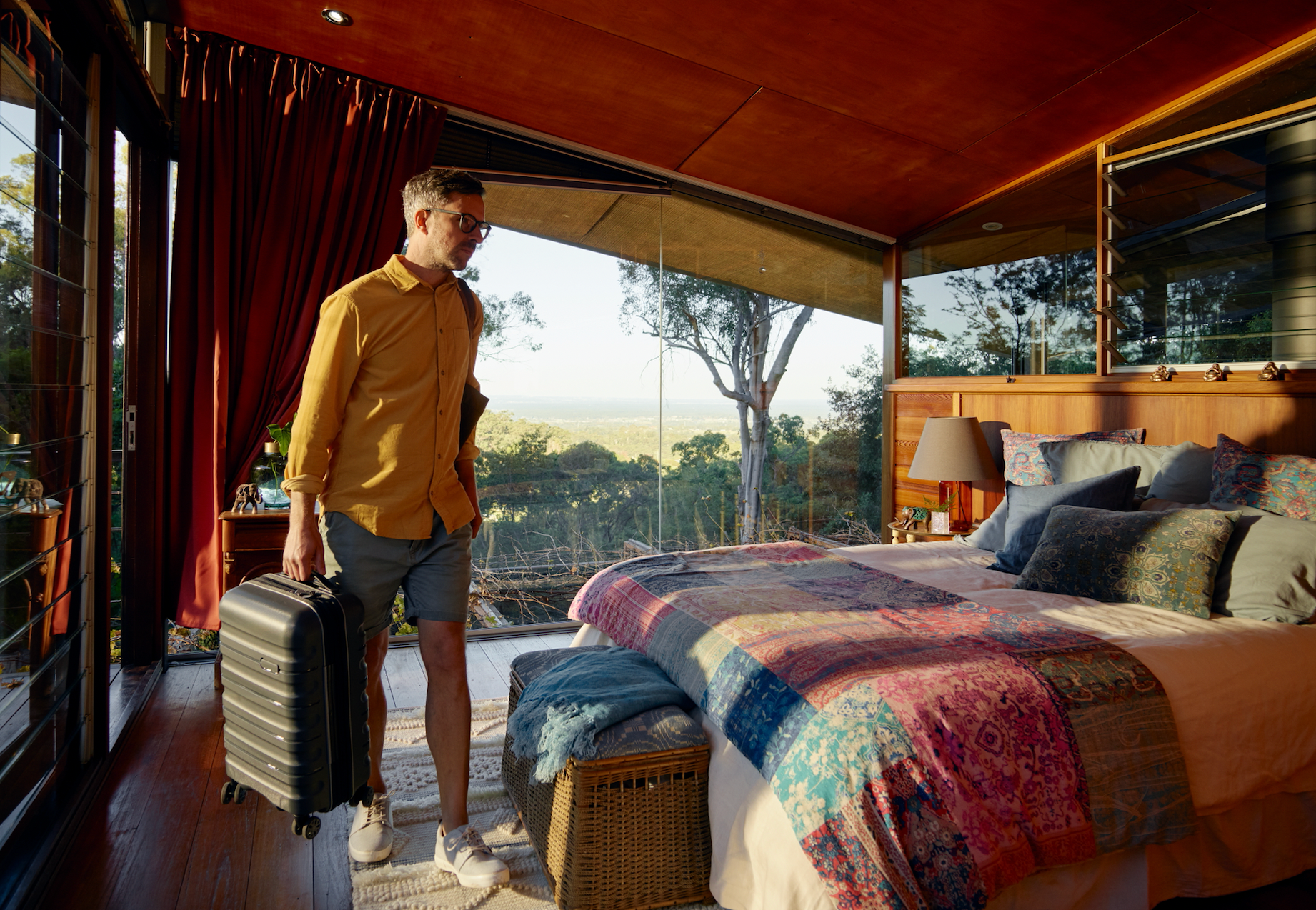 한 사람이 창문 너머로 녹음 가득한 풍경이 보이는 넓은 침실에서 여행 가방을 들고 있습니다.