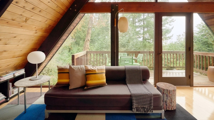 En el centro de la habitación superior de una casa alpina, hay un sillón bien arreglado con tres almohadones y una manta.