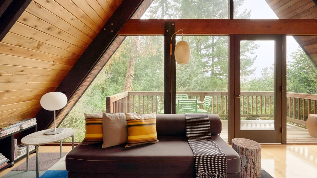 En el centro de la habitación superior de una casa alpina, hay un sillón bien arreglado con tres almohadones y una manta.