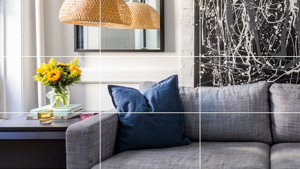 一张带网格的手机图片，显示的是客厅中的一张灰色沙发，沙发旁边的茶几上摆着一些向日葵。