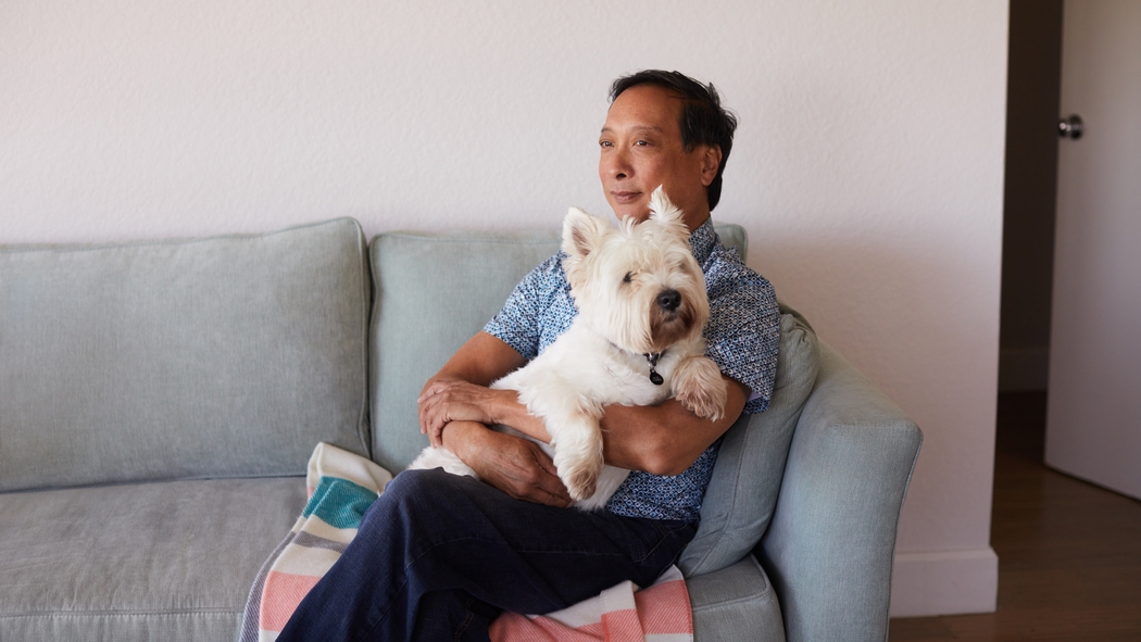 A person sits on a blue sofa holding a white fluffy dog.