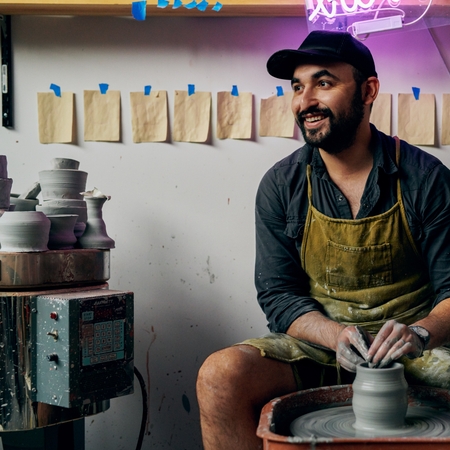 Un participant la experiență care zâmbește în timpul realizării unui obiect ceramic pe o roată de olărit.