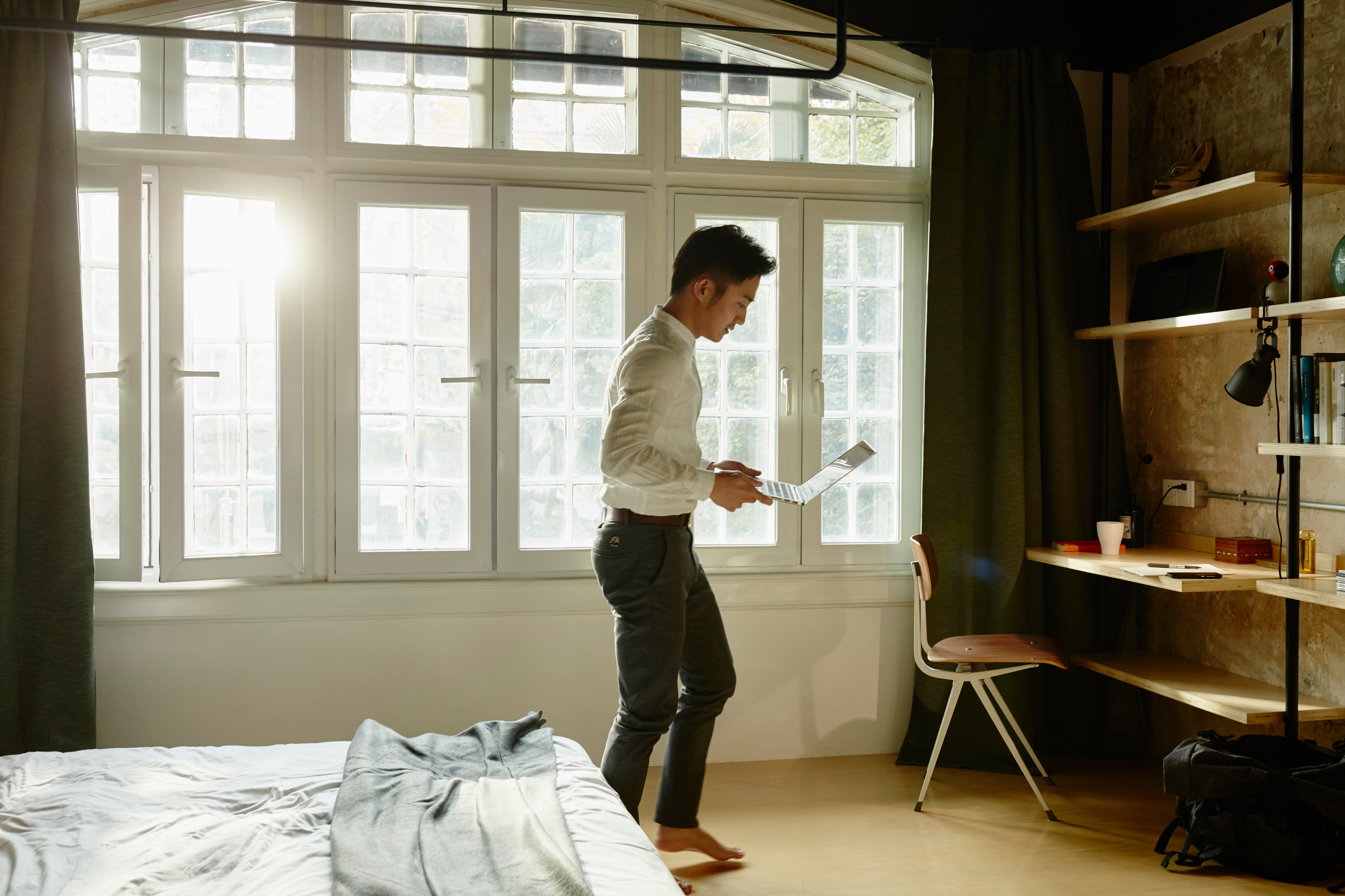 Maður stendur í sólríku svefnherbergi og horfir á símann sinn með stóran glugga fyrir aftan sig.