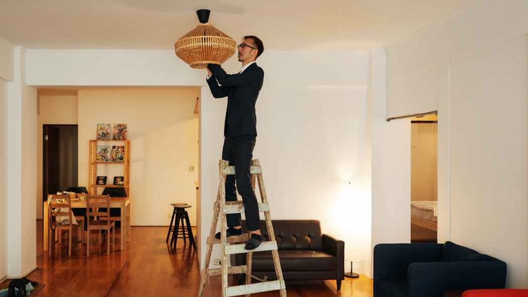 A man stands on a ladder while installing a chandelier.