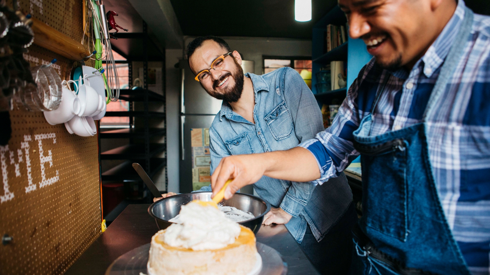 Un voyageur fait le glaçage d'un gâteau pendant que l'hôte regarde et sourit